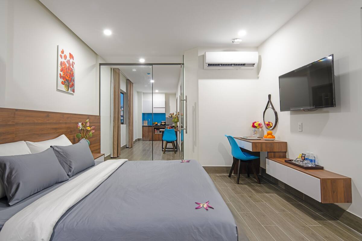 Quarto de hotel moderno com cama, escrivaninha, cadeira, televisão e ar condicionado.