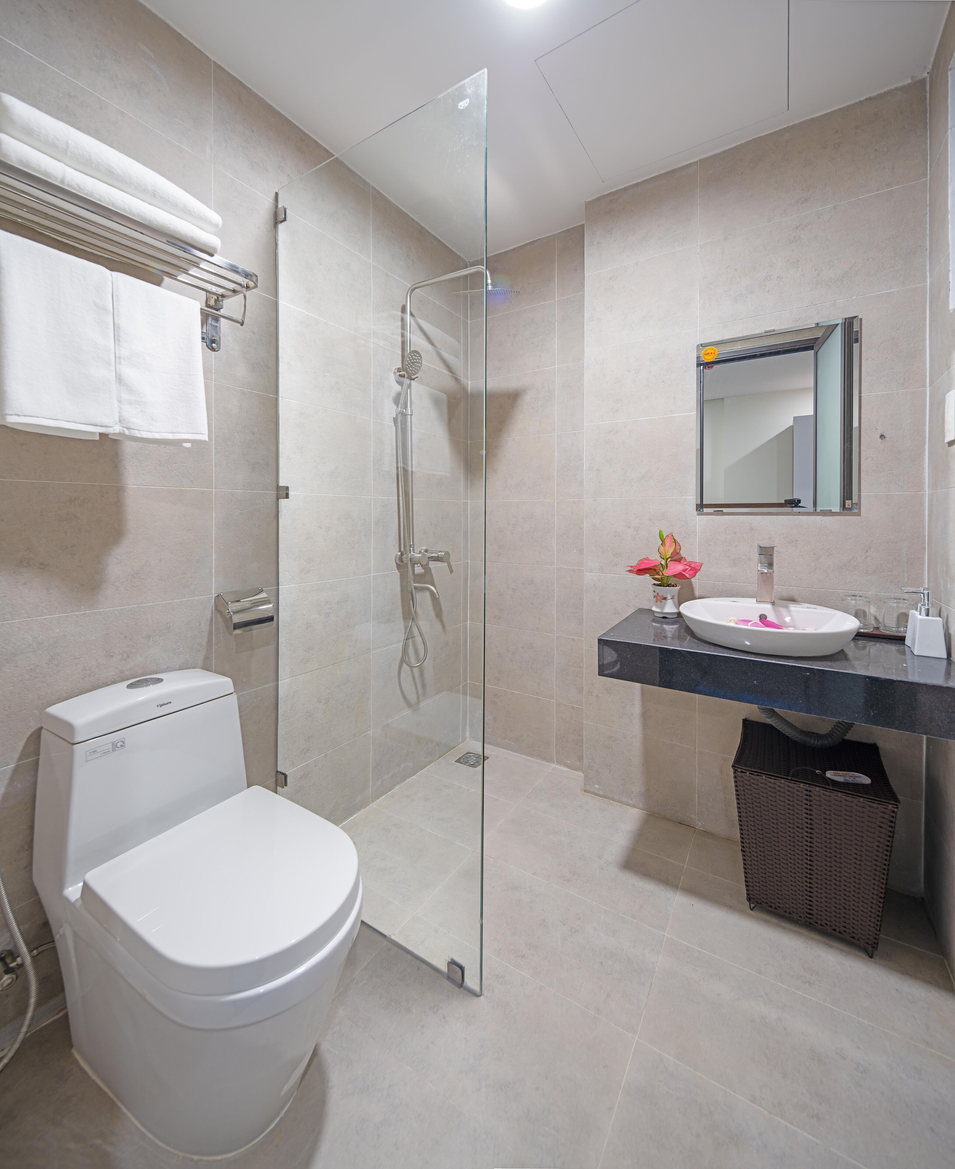Un baño moderno con ducha de vidrio, inodoro blanco, lavabo con espejo y una cesta.