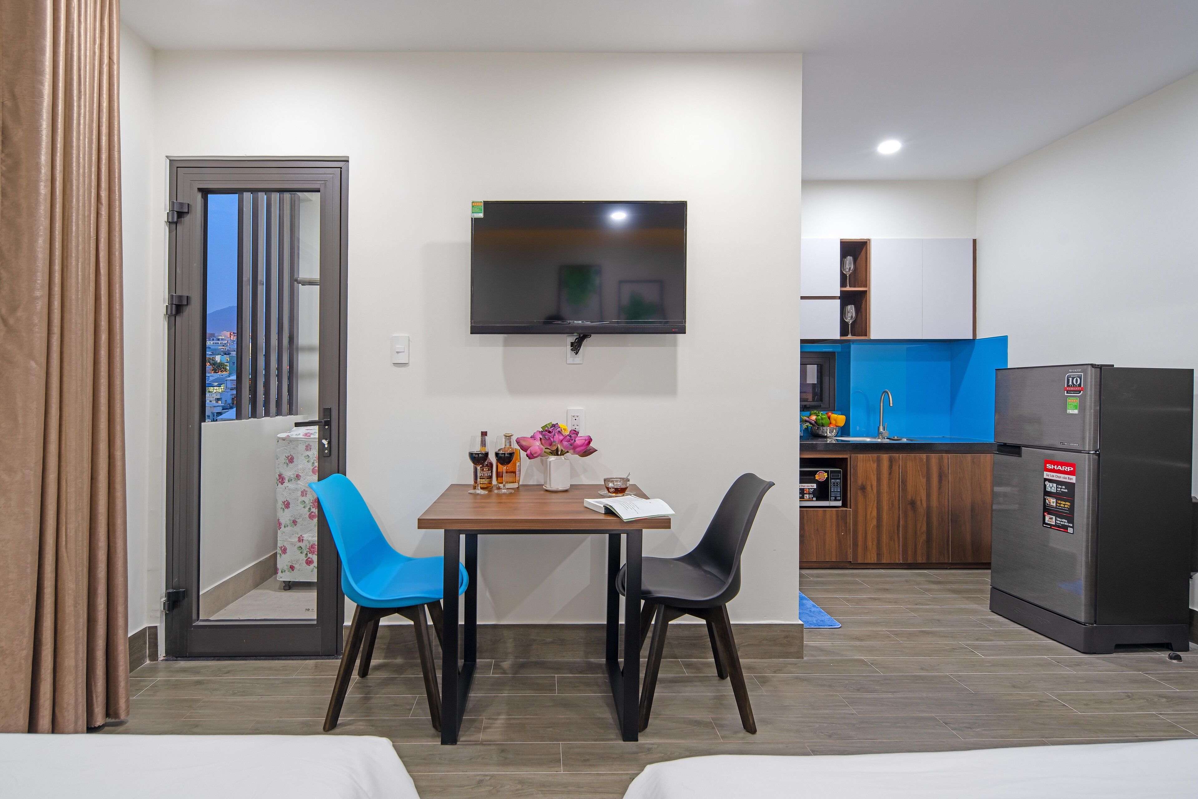 Une chambre d’hôtel compacte comprenant un coin repas, un téléviseur fixé au mur, un réfrigérateur et une vue sur l’extérieur, accessible par une porte.