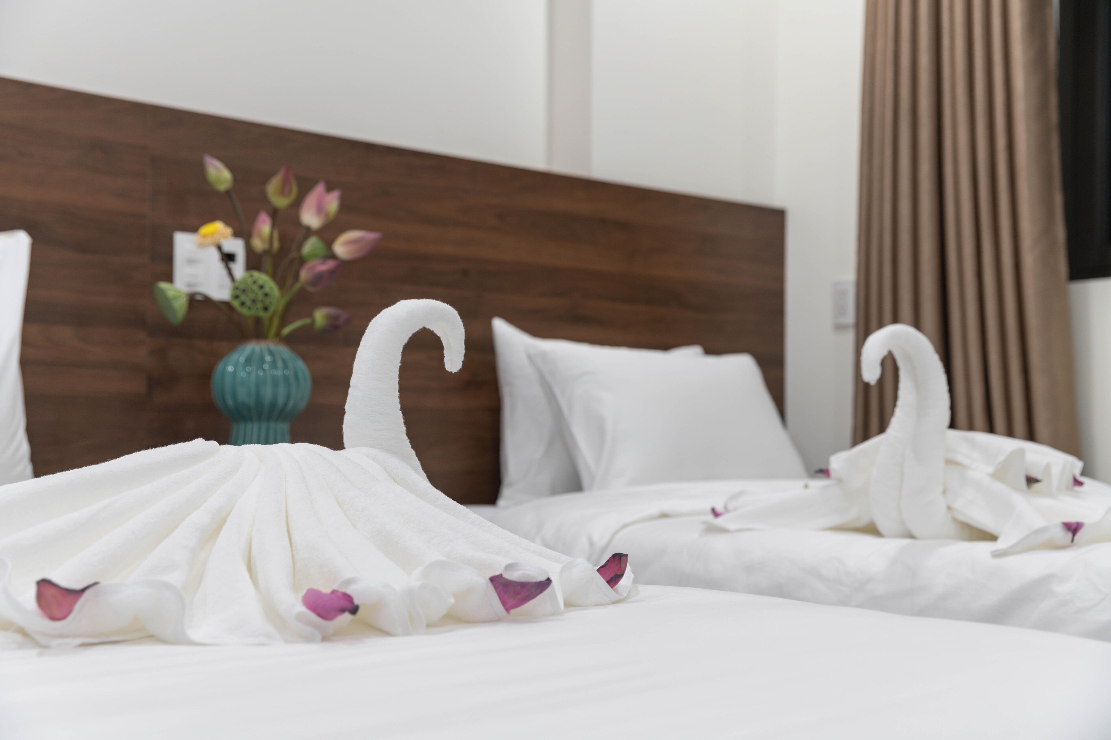 A hotel room with a wooden headboard, white bedding, and decorative swan-shaped towels.