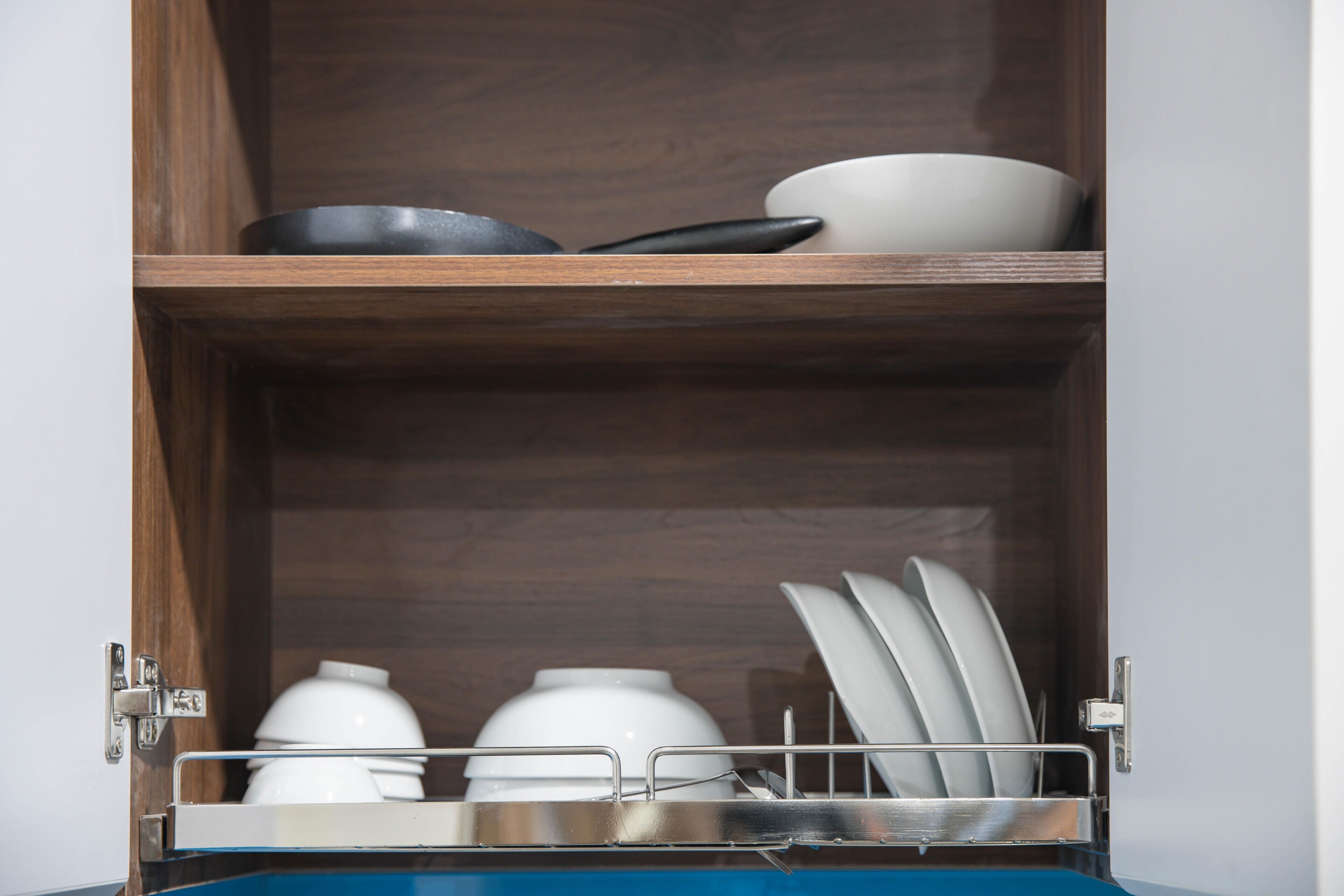 A wooden cabinet with shelves holding various kitchenware, including bowls, plates, and a pan.