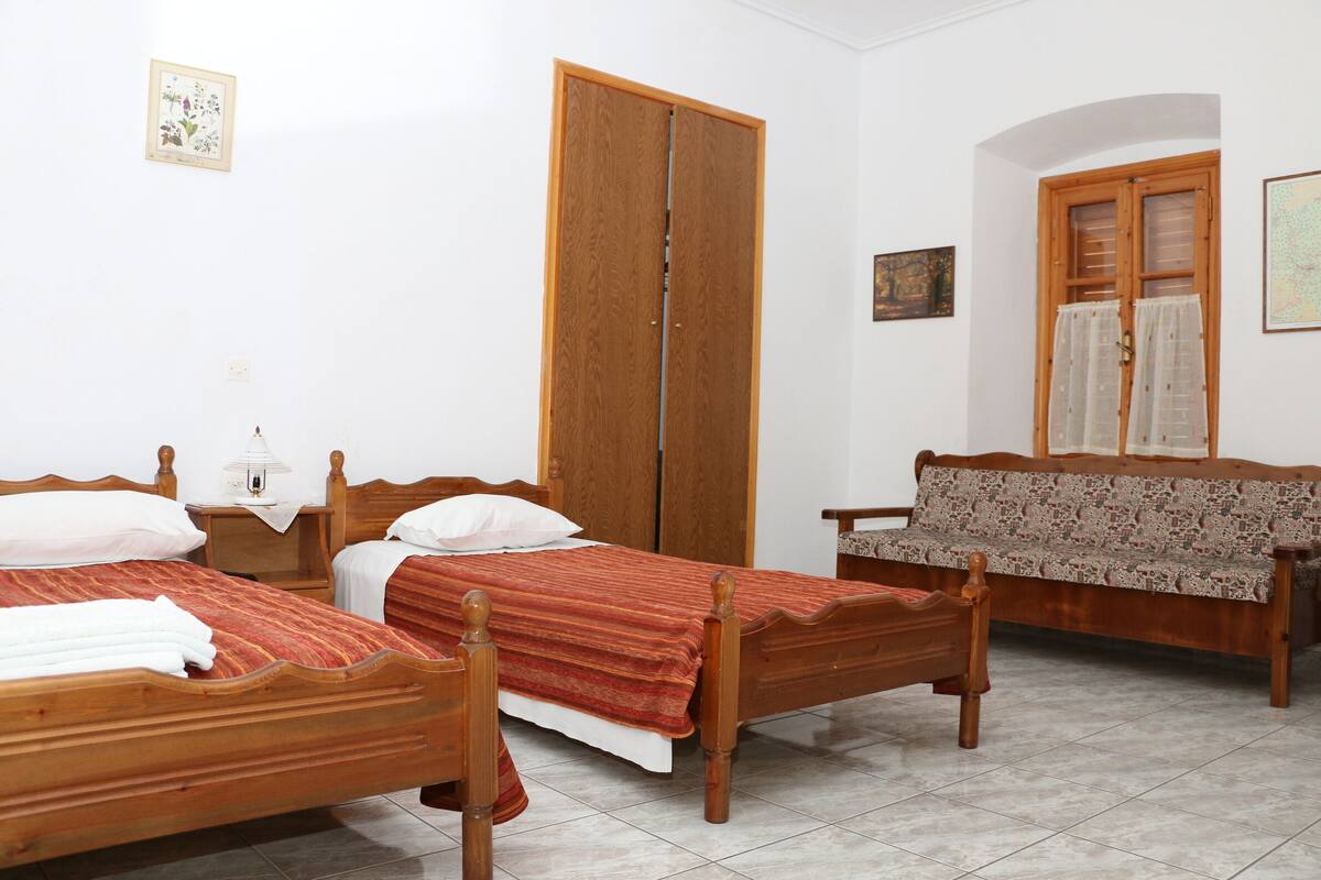 Un dormitorio con dos camas de madera, un armario de madera, un banco y una ventana con cortinas.