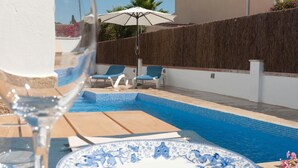 Una piscina con azulejos azules, sillas de descanso y una mesa de vidrio con un plato.
