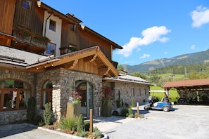 A stone building with a wooden facade, a balcony with red flowers, and a golf cart in the parking area. - Hotel am Schloss (Goldegg)