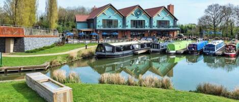 A riverside hotel with a docked boat, a grassy area, and a stone wall.