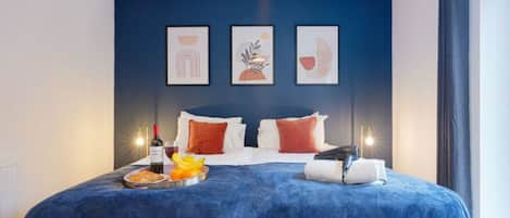 A hotel room with a large bed, a tray with breakfast items, and three framed artworks on the wall.