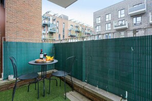 Un pequeño patio al aire libre con una mesa, sillas, una botella de vino y fruta.