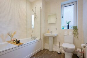 Un baño con bañera, lavamanos, inodoro y ventana con plantas.