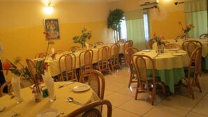 A dining area with multiple round tables covered with yellow tablecloths, wooden chairs, and floral centerpieces. - Lamonde Guest House (Owerri)