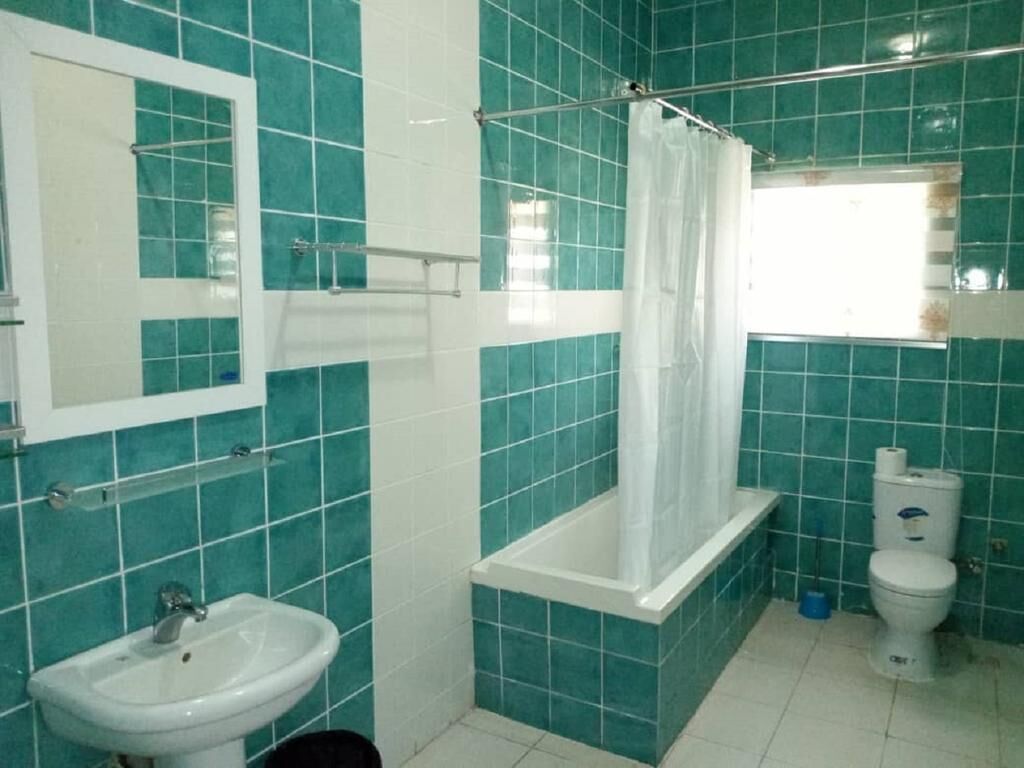 Un baño con azulejos color turquesa, un lavabo blanco, una bañera con cortina de ducha y un inodoro.