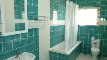Un baño con azulejos color turquesa, un lavabo blanco, una bañera con cortina de ducha y un inodoro.