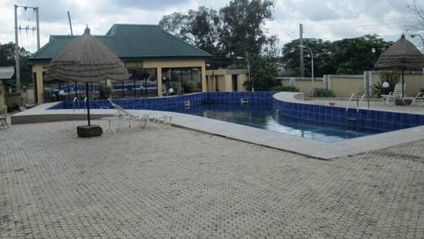 A swimming pool with a blue tiled border, surrounded by a paved area with umbrellas and lounge chairs. - Lamonde Guest House (Owerri)