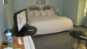 A hotel room with a bed, a TV on a desk, a table, and a chair. - Lamonde Guest House (Owerri)