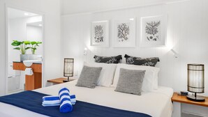 A modern hotel room with a large bed, a bedside table with a lamp, a nightstand, and a mirror. There are three framed botanical prints on the wall above the bed. - 14 Alamanda Resort  - Where Pure Luxury meets the Coral Sea (Palm Cove)