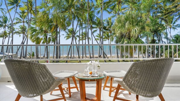 A balcony with wicker chairs and a glass table, overlooking a beach with palm trees and the ocean. - 14 Alamanda Resort  - Where Pure Luxury meets the Coral Sea (Palm Cove)
