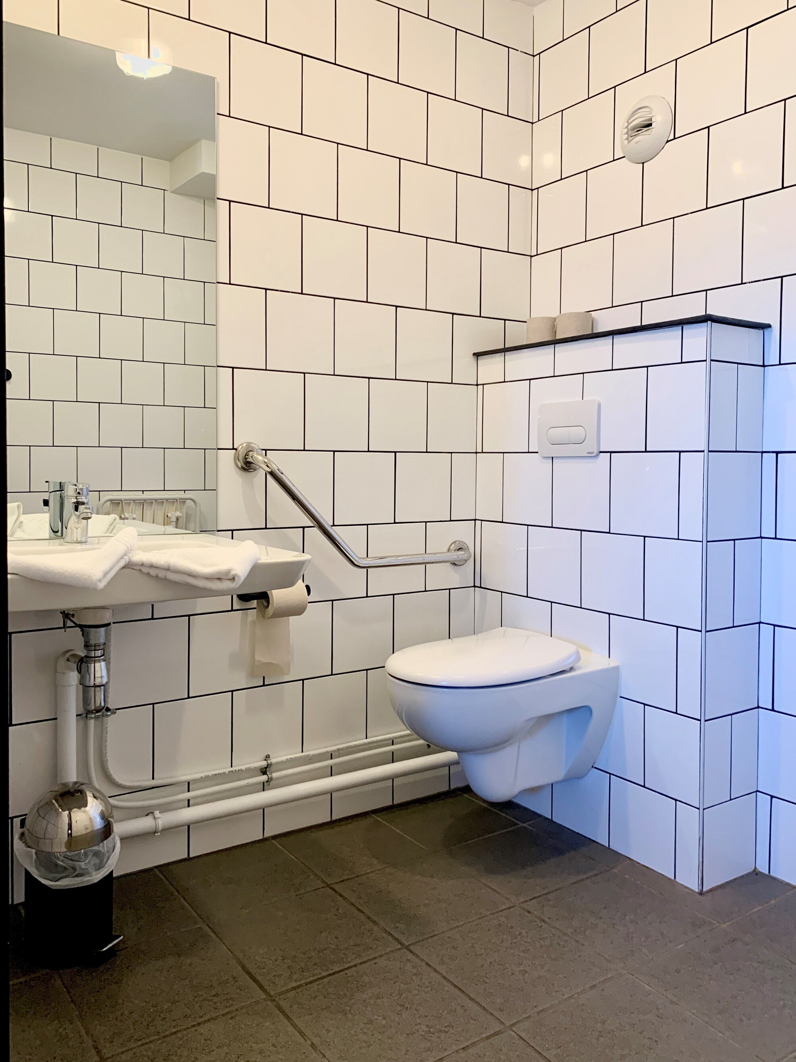 Et moderne badeværelse med hvide flisevægge, en hvid vask og et toilet.