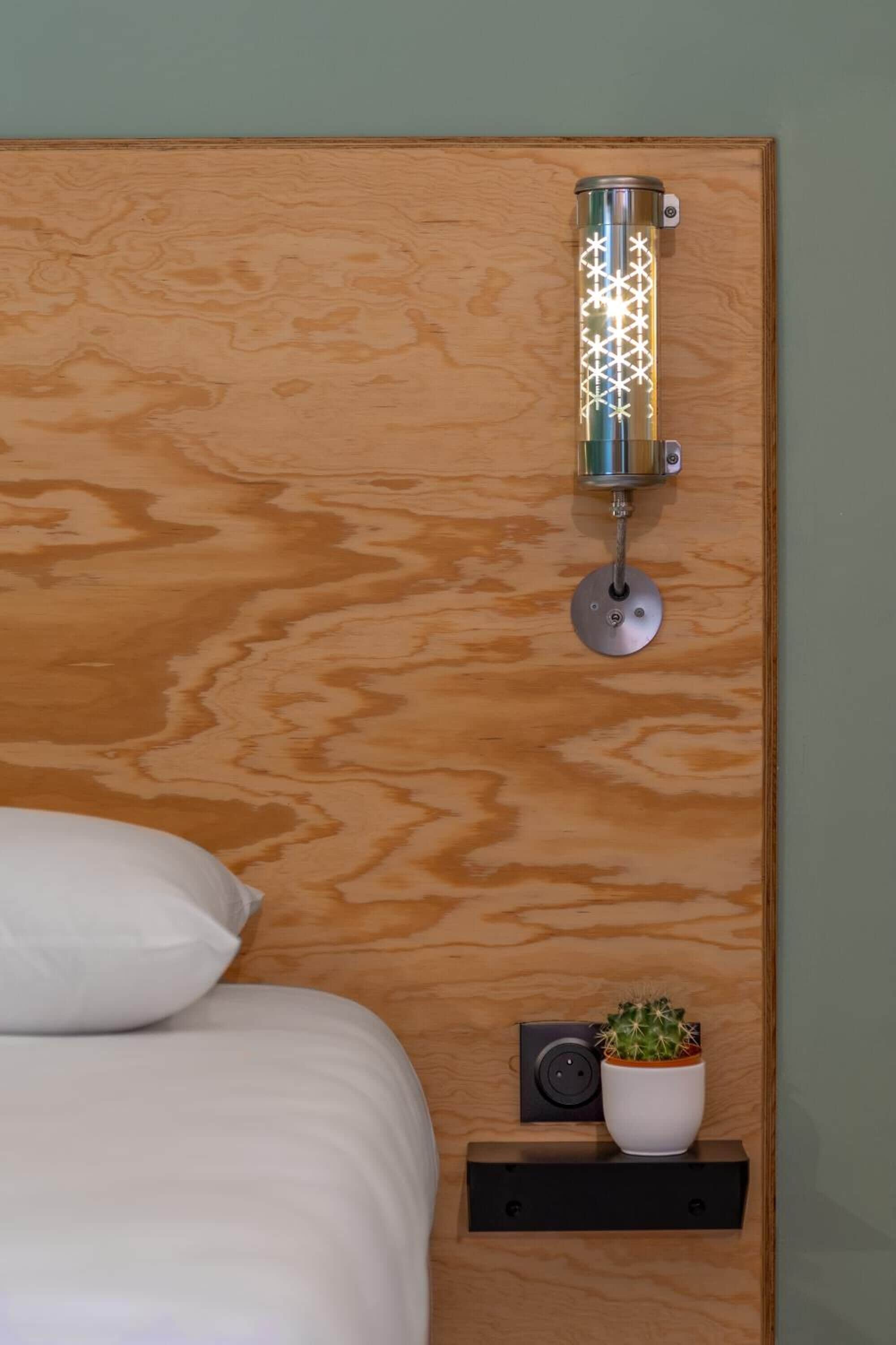 A wooden headboard with a wall-mounted light fixture and a small shelf with a potted plant.