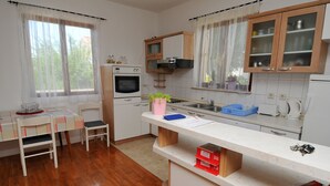 Une cuisine équipée d’une table à manger, de chaises, d’un plan de travail, de placards et d’une fenêtre avec des rideaux.