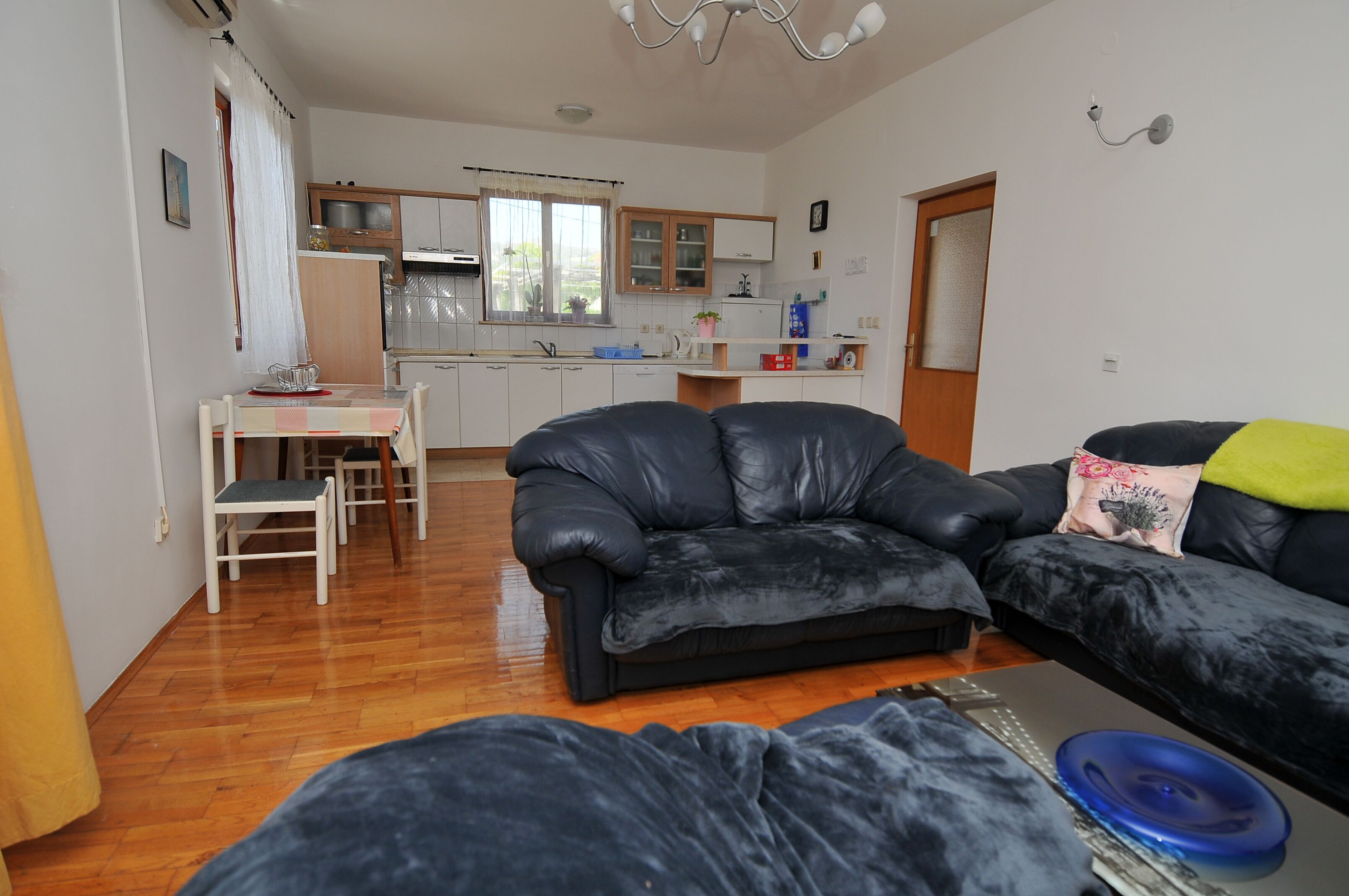 Ein Wohnzimmer mit einer schwarzen Ledersofa, einem Esstisch mit Stühlen und einer Küche im Hintergrund.