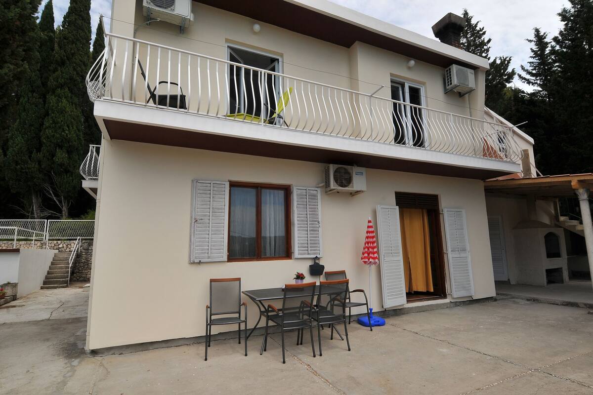Un bâtiment à deux étages doté d’un balcon, d’une table avec des chaises et d’une porte avec des volets.