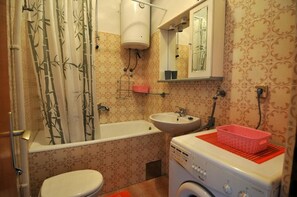 Casa de banho com banheira, sanita, lavatório e máquina de lavar roupa.