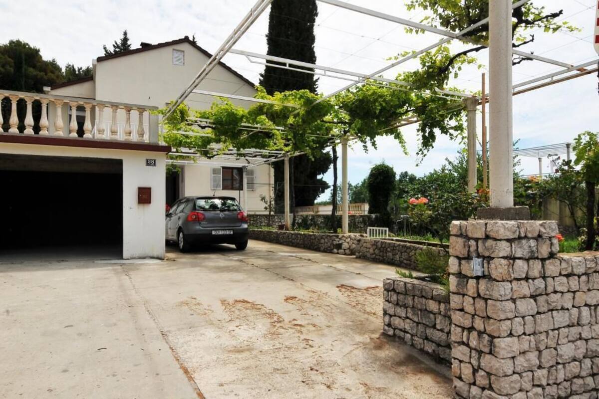 Un garage attenant à une maison, avec une voiture garée à l’intérieur, un mur en pierre et une pergola couverte de plantes grimpantes.