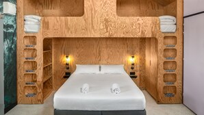 Une chambre à coucher avec une tête de lit en bois, deux tables de chevet avec des lampes, un lit avec une literie blanche et une fresque murale sur le thème de la forêt.