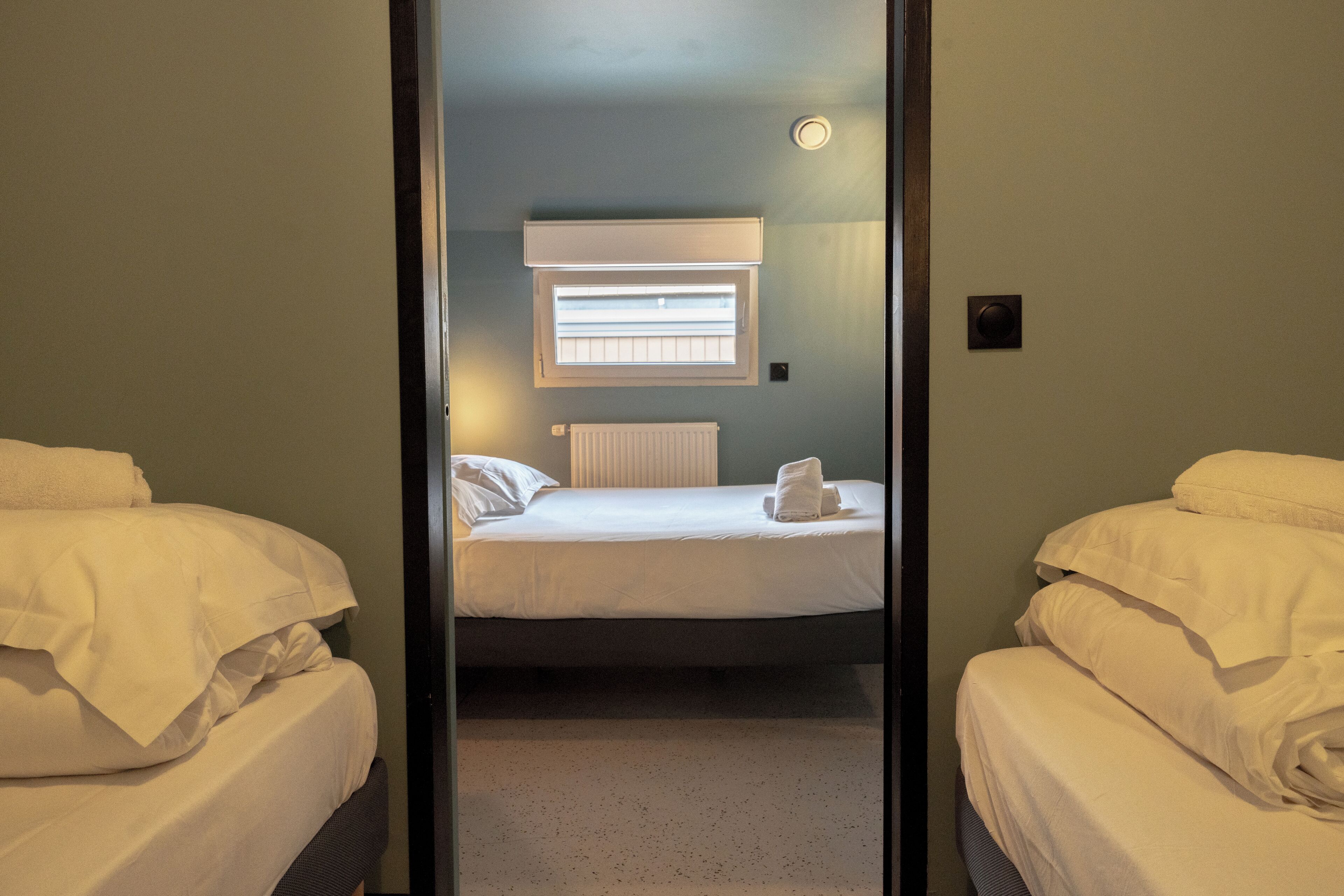 A hotel room with two beds, a window with blinds, a radiator, and a towel on one bed.