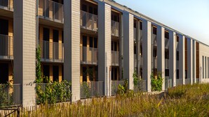 Un bâtiment moderne à plusieurs étages, doté de balcons, d’un toit plat et d’un parterre verdoyant.