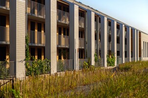 Un bâtiment moderne à plusieurs étages, doté de balcons, d’un toit plat et d’un parterre verdoyant.
