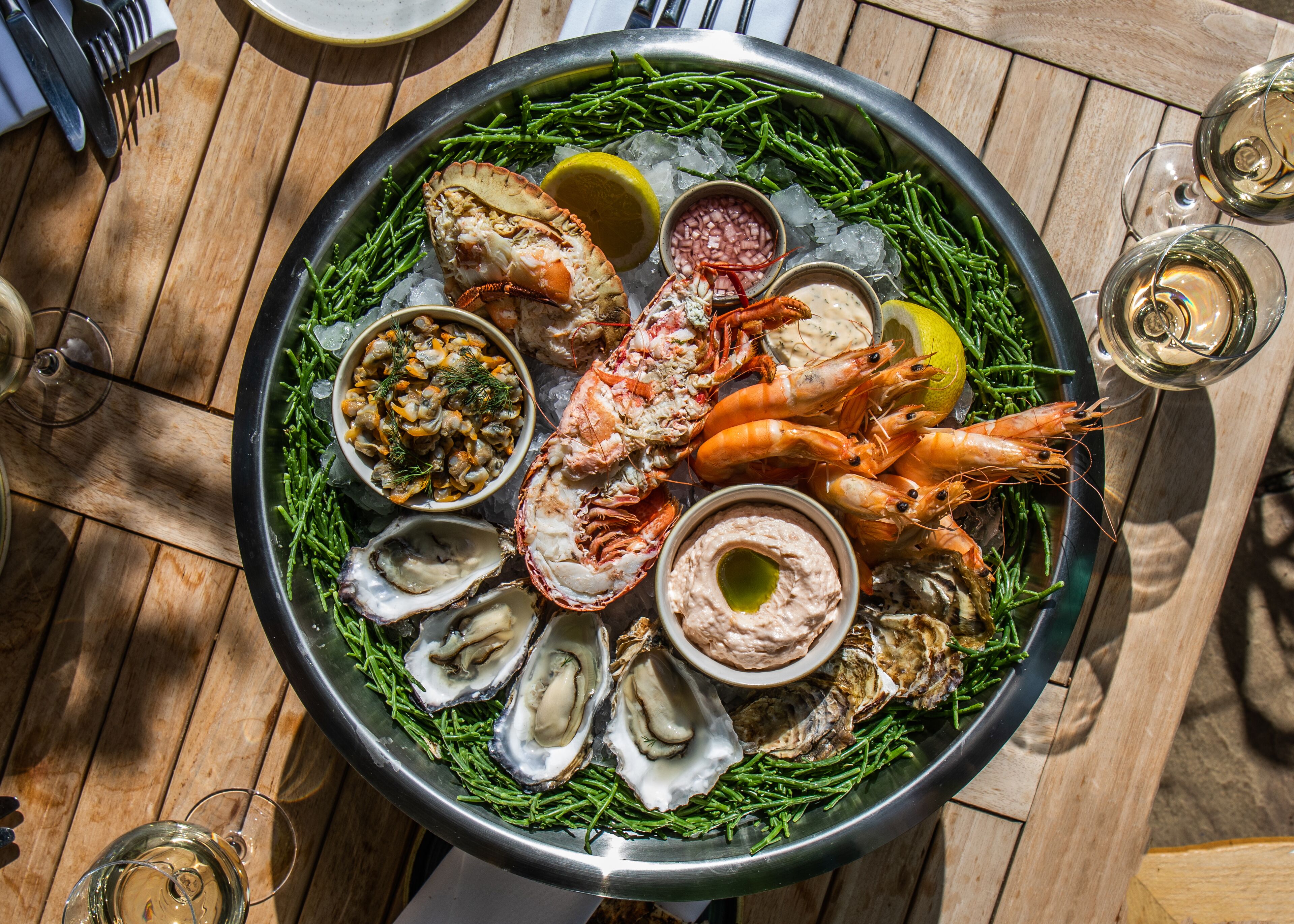 Un plateau de fruits de mer composé d’huîtres, de crevettes et de homard, disposés sur un lit de glace, accompagné de quartiers de citron et de sauces pour tremper.