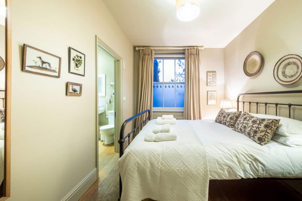 Un dormitorio con cama, cortinas en la ventana, una mesita de noche y obras de arte colgadas en la pared.