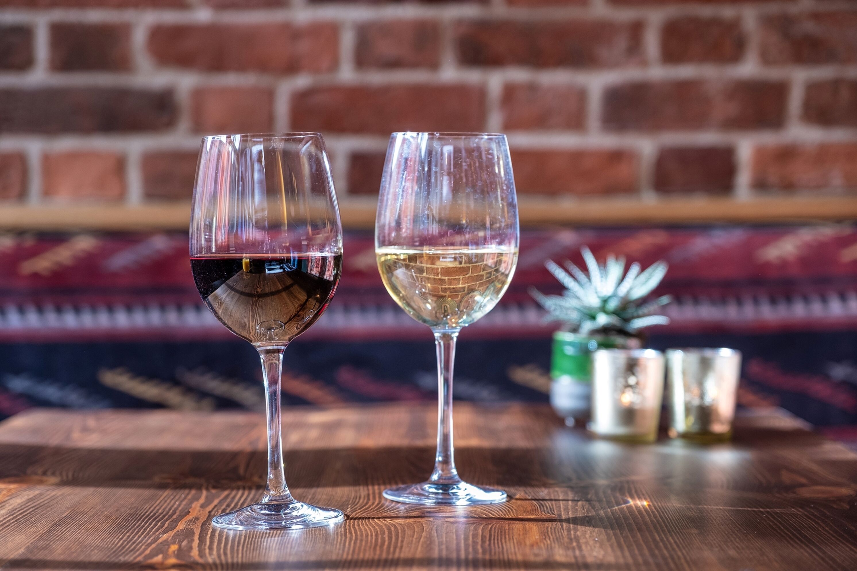 Two wine glasses on a wooden table with a brick wall background.