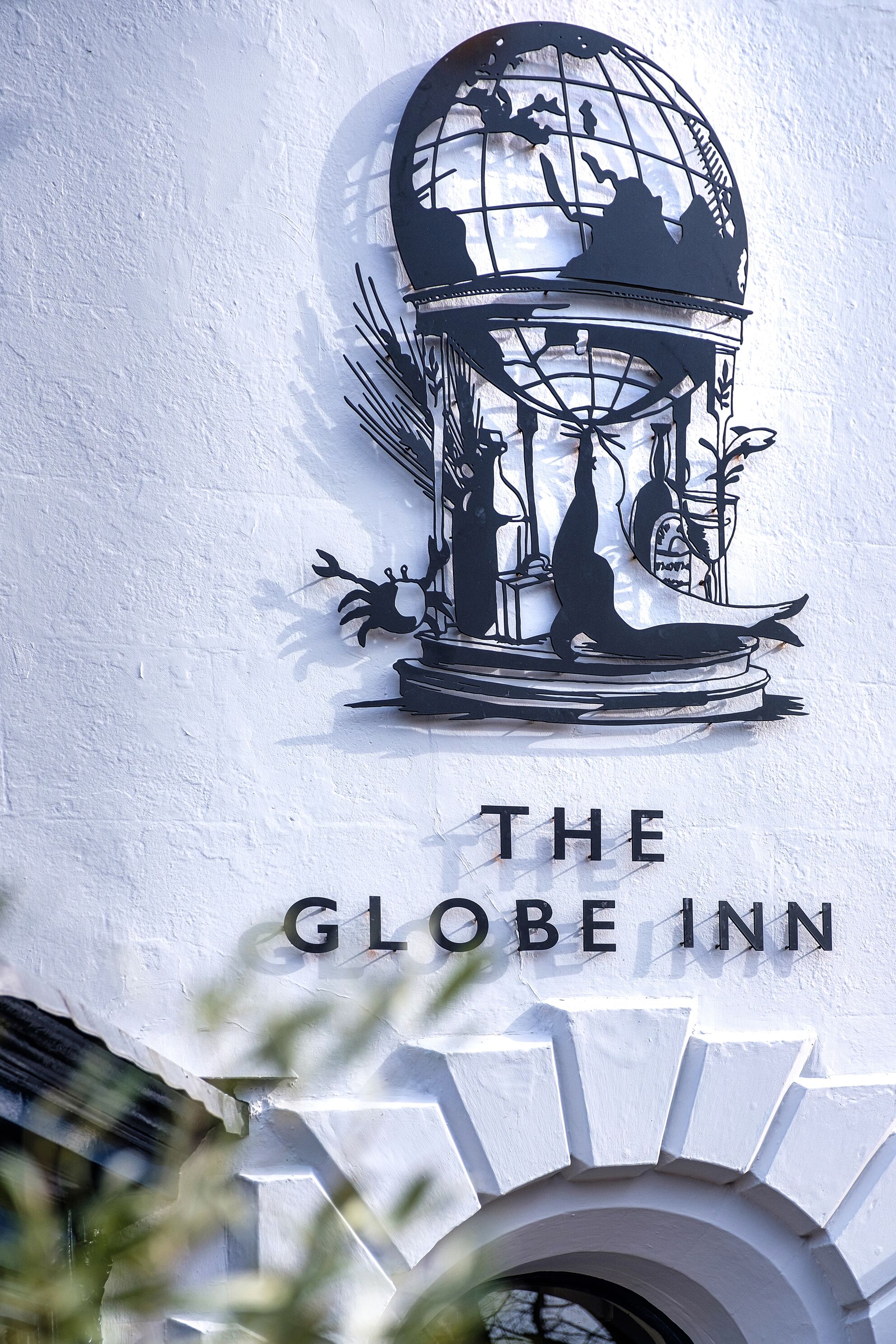 Un letrero en la pared del The Globe Inn que presenta un globo terráqueo con siluetas de un barco, una ballena y un faro.