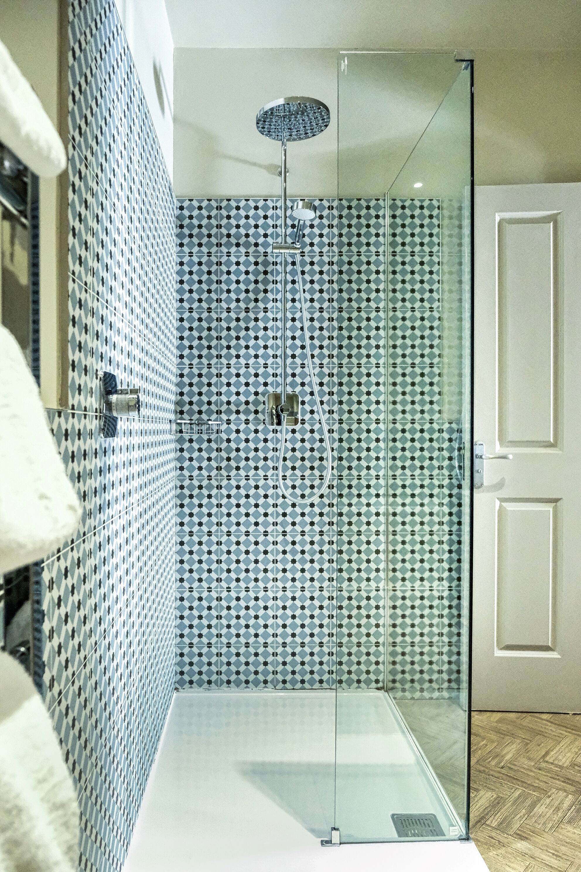 Un baño moderno con cabina de ducha de vidrio, paredes revestidas de azulejos y suelo de madera.
