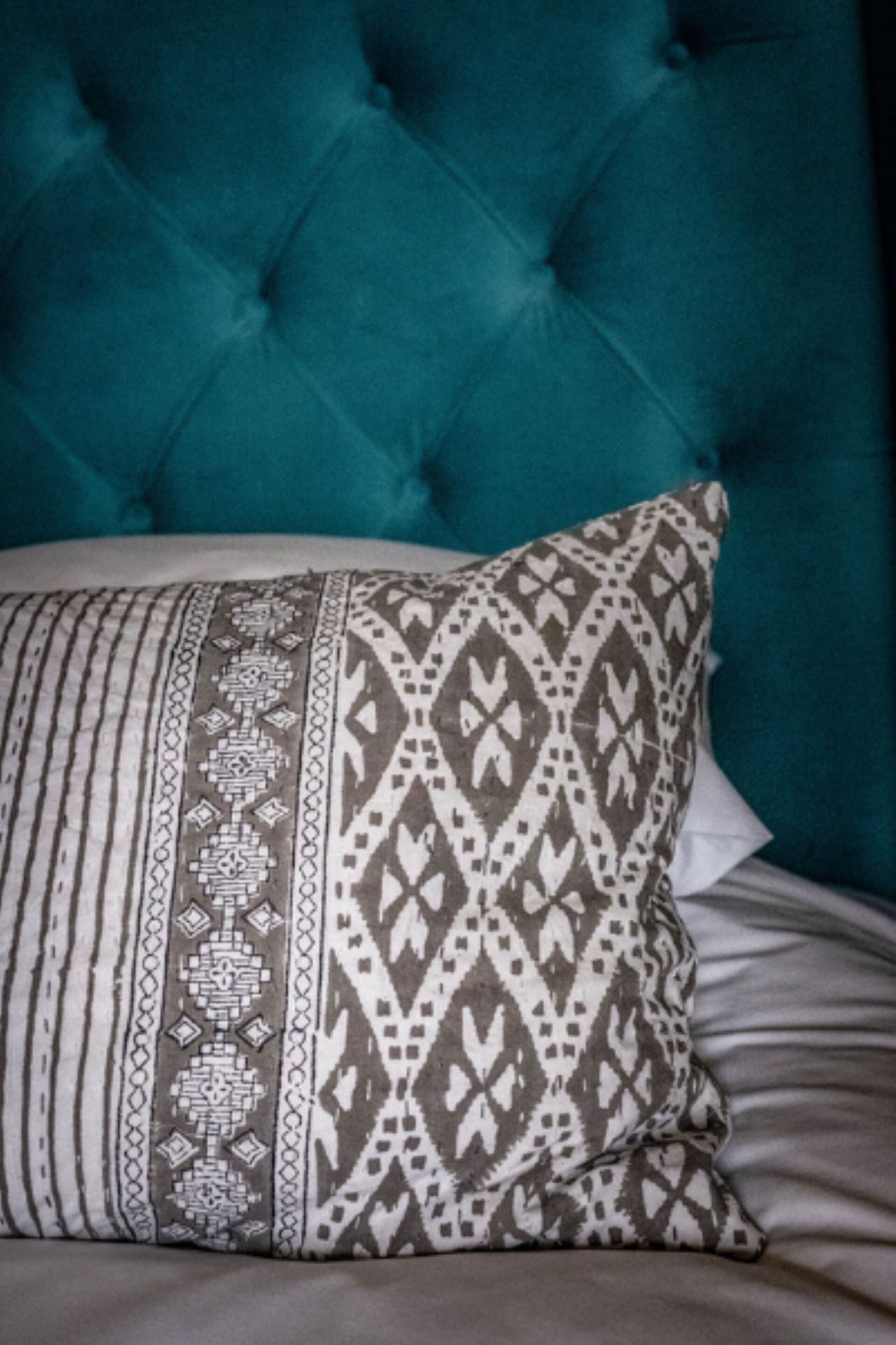 Cabecera tapizada en color turquesa con un cojín estampado sobre la cama.