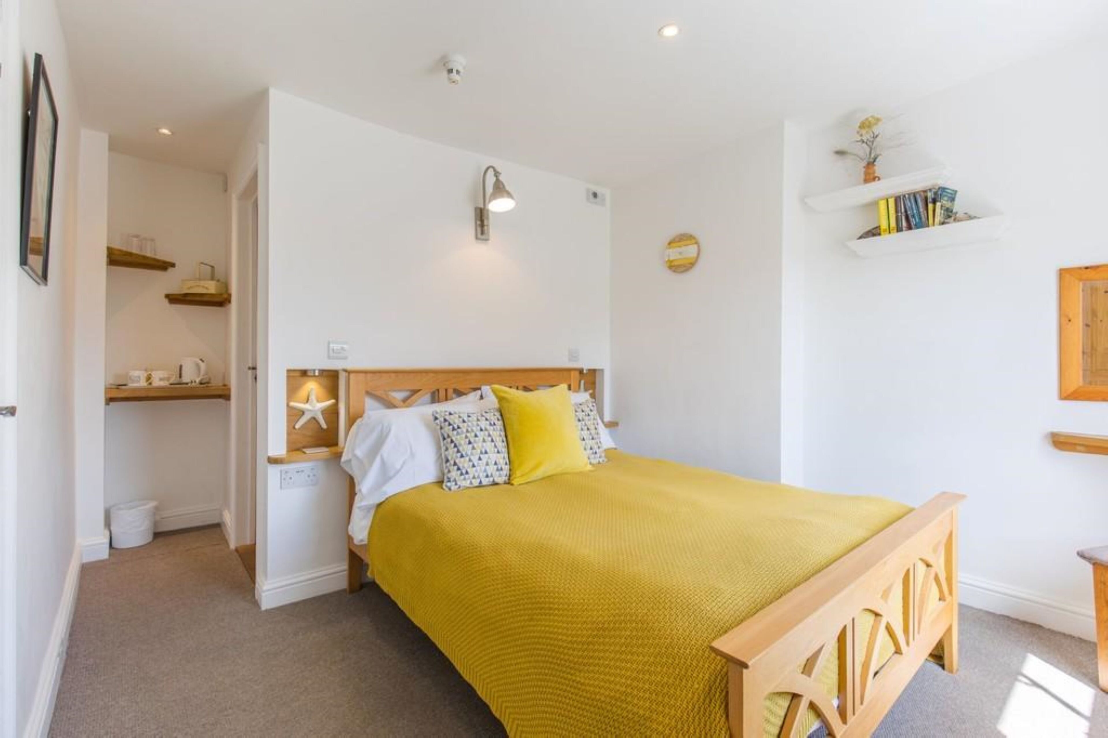 Un dormitorio con una cama de madera, una colcha amarilla, una decoración con forma de estrella de mar y una estantería con libros y una pequeña planta.