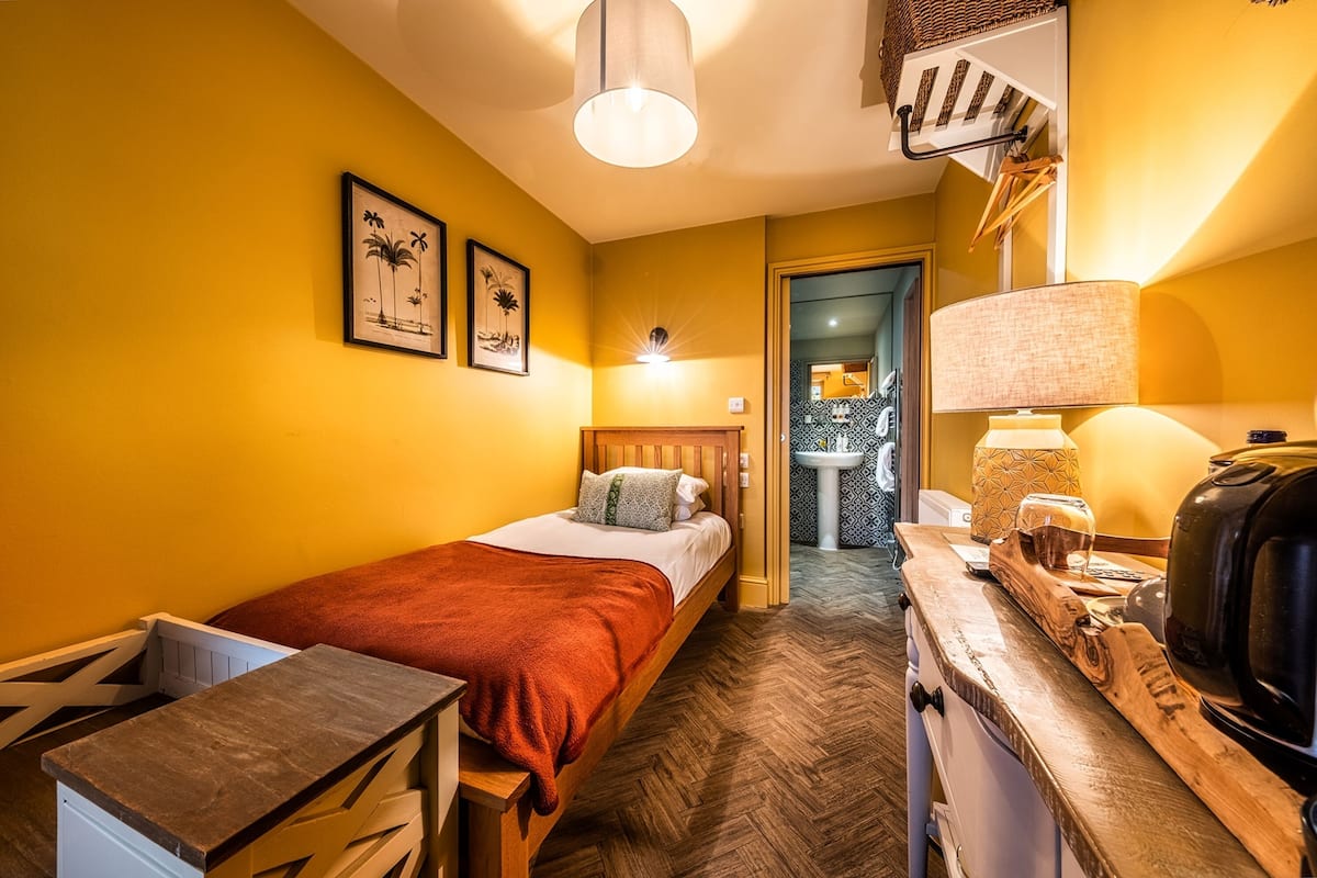 Habitación de hotel con una cama, un escritorio de madera, una lámpara y una cafetera.
