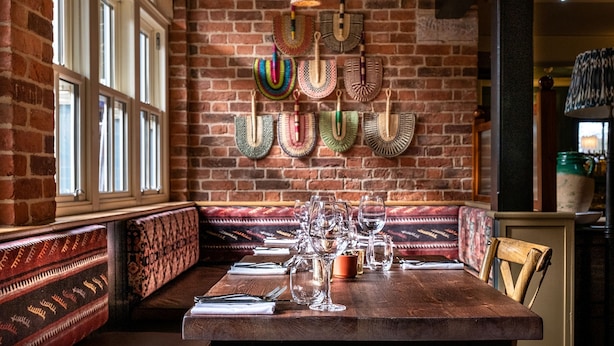 A dining area with a brick wall, patterned benches, and a table set with wine glasses and cutlery. - The Globe Inn Wells (Wells-next-the-Sea)