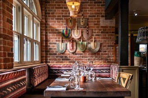 Un comedor con pared de ladrillo, bancos estampados y una mesa dispuesta con copas de vino y cubiertos.