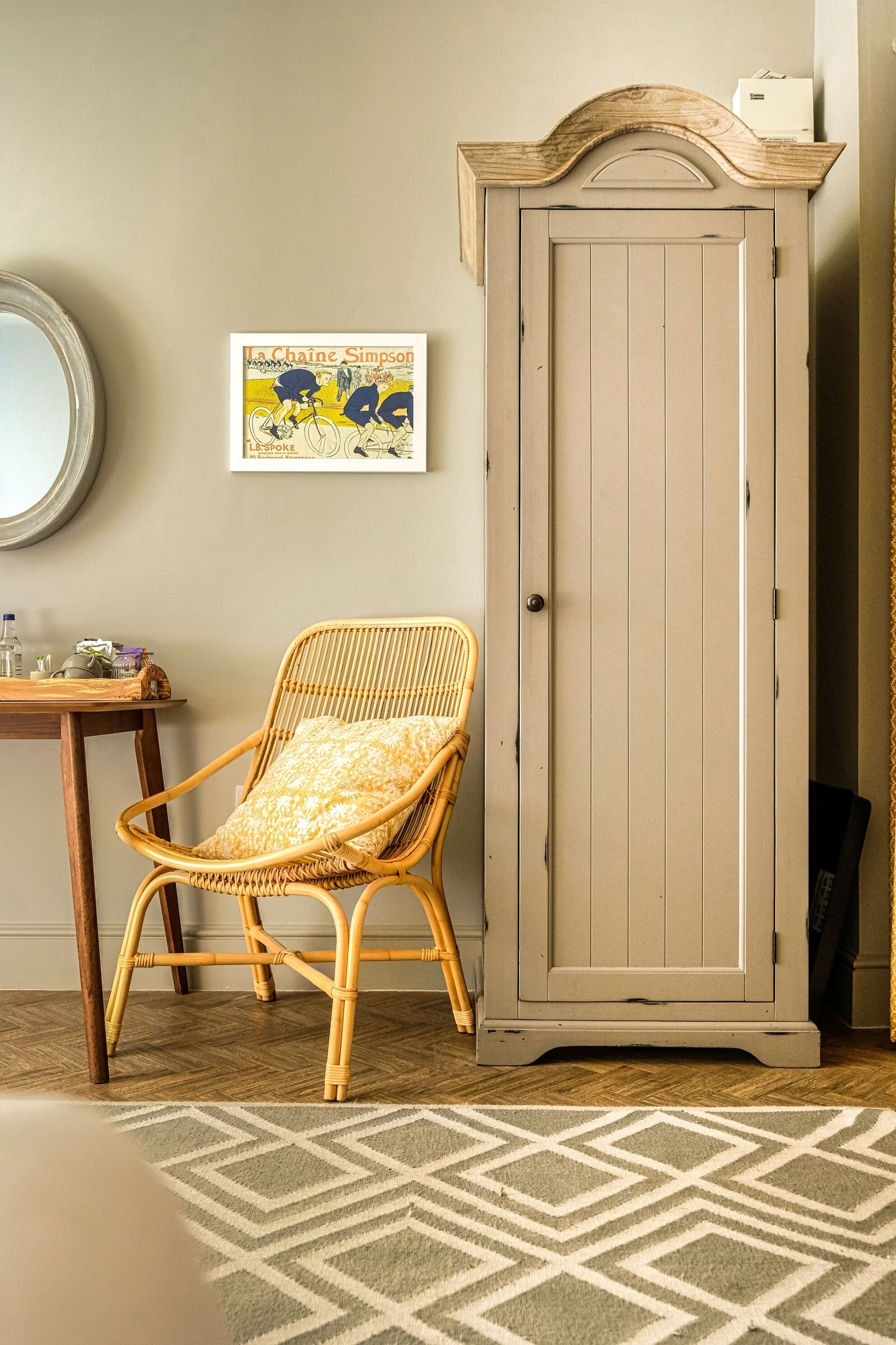 Une pièce comprenant un fauteuil en osier, une armoire, un tableau encadré et un tapis à motifs.