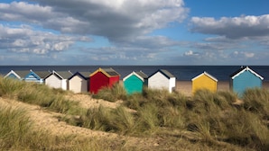 A row of colorful beach huts along a sandy beach with the sea in the background. - The Globe Inn Wells (Wells-next-the-Sea)