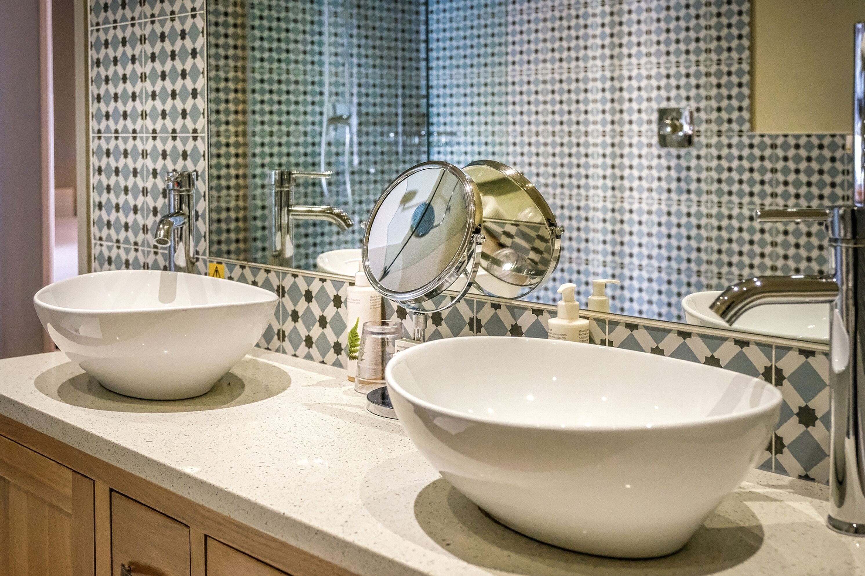 Une salle de bain avec deux grands lavabos blancs, un miroir et un mur recouvert de carreaux décoratifs.