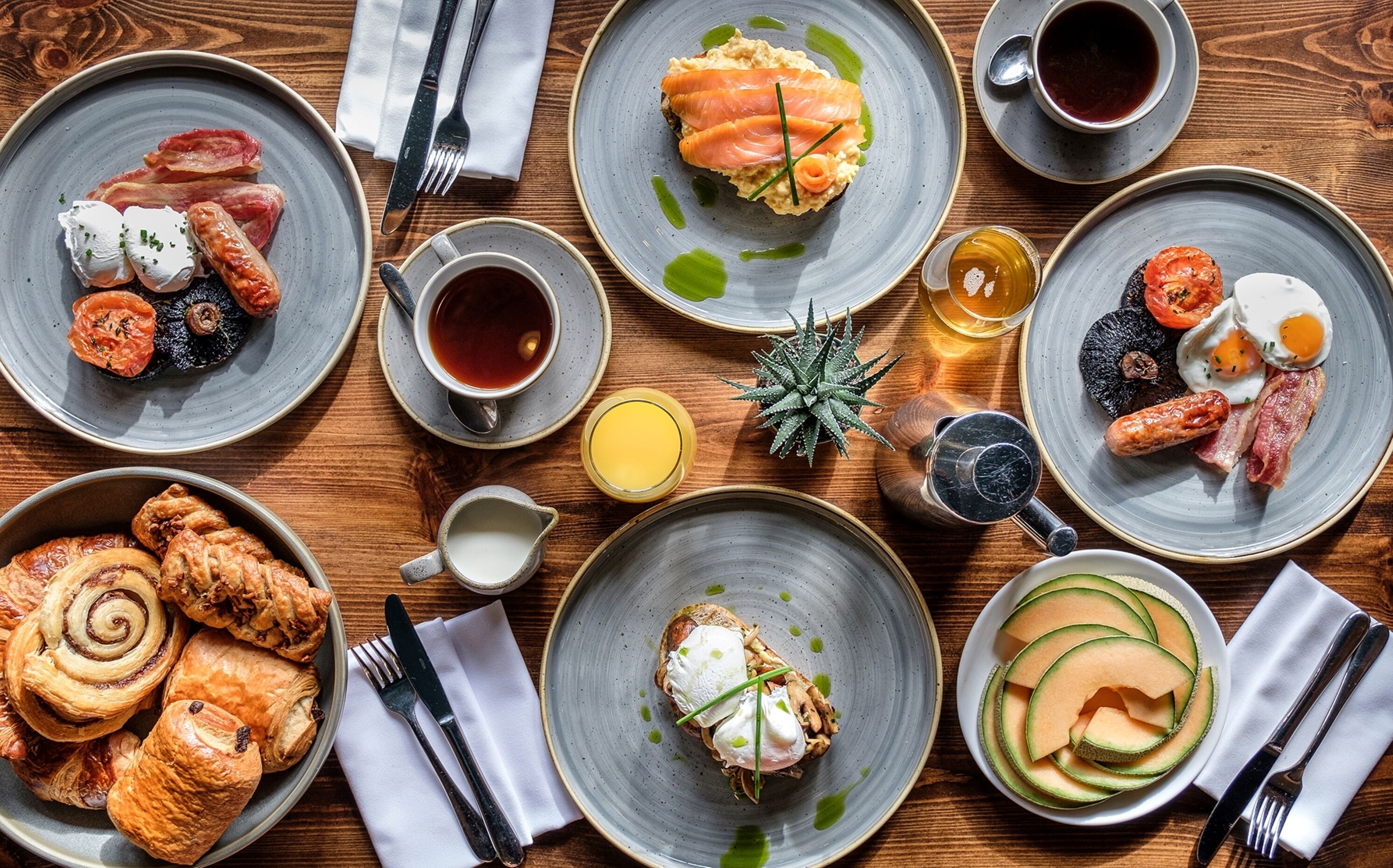 A variety of breakfast dishes including eggs, bacon, smoked salmon, and pastries on a wooden table.