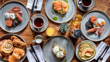 A variety of breakfast dishes including eggs, bacon, smoked salmon, and pastries on a wooden table.