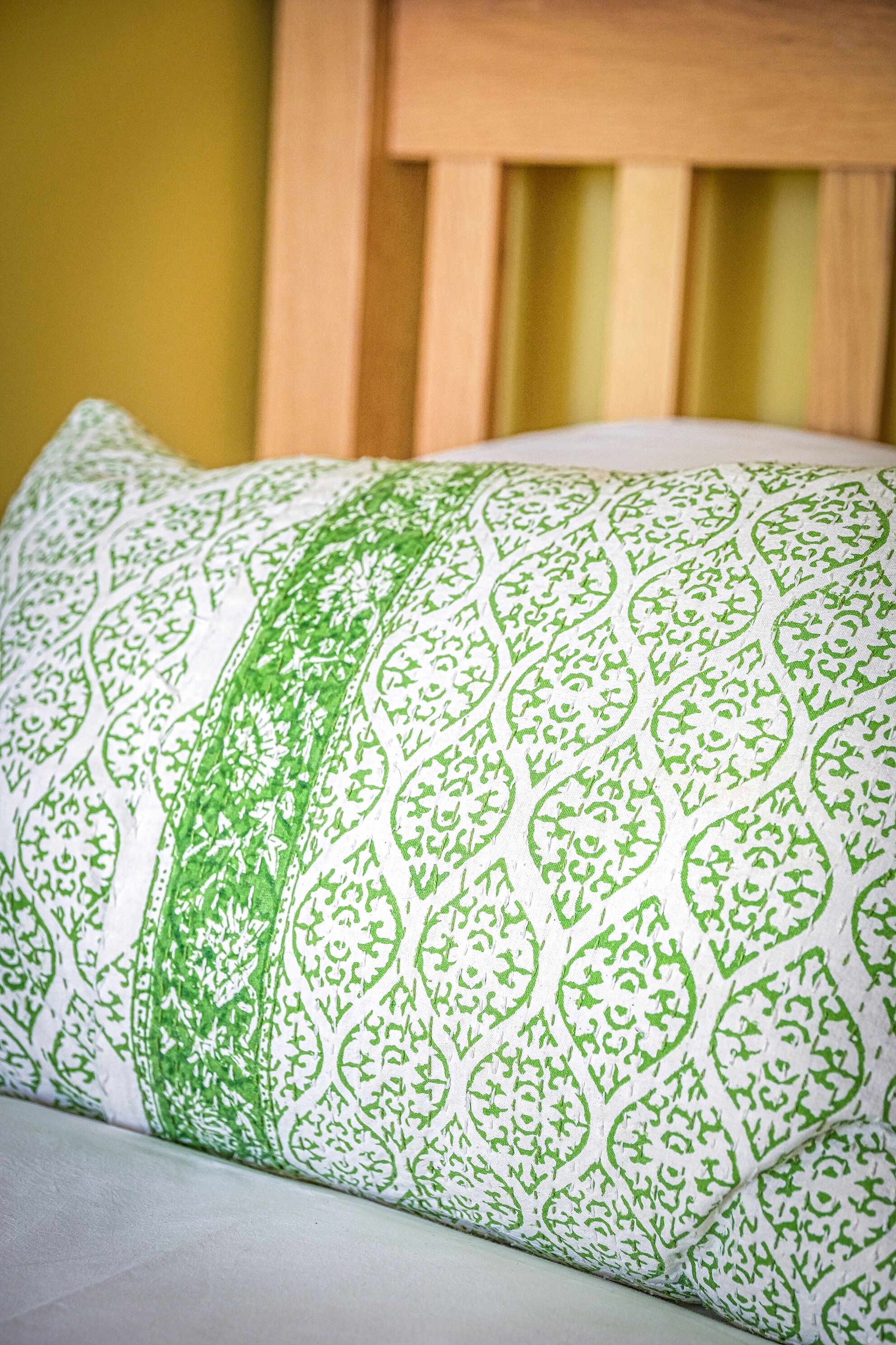Un almohadón con un estampado verde y blanco sobre una cama.