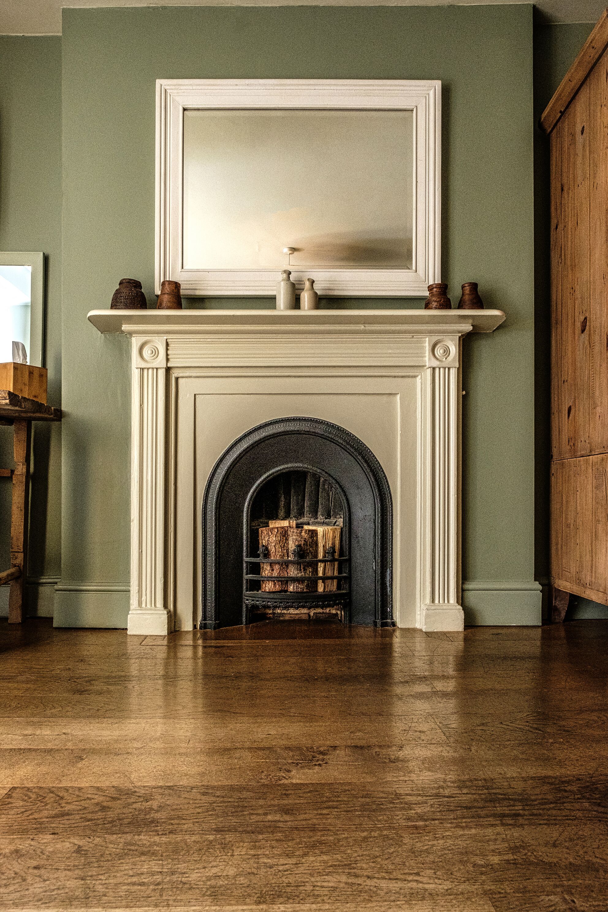 Una chimenea con repisa, suelo de madera y pared verde.