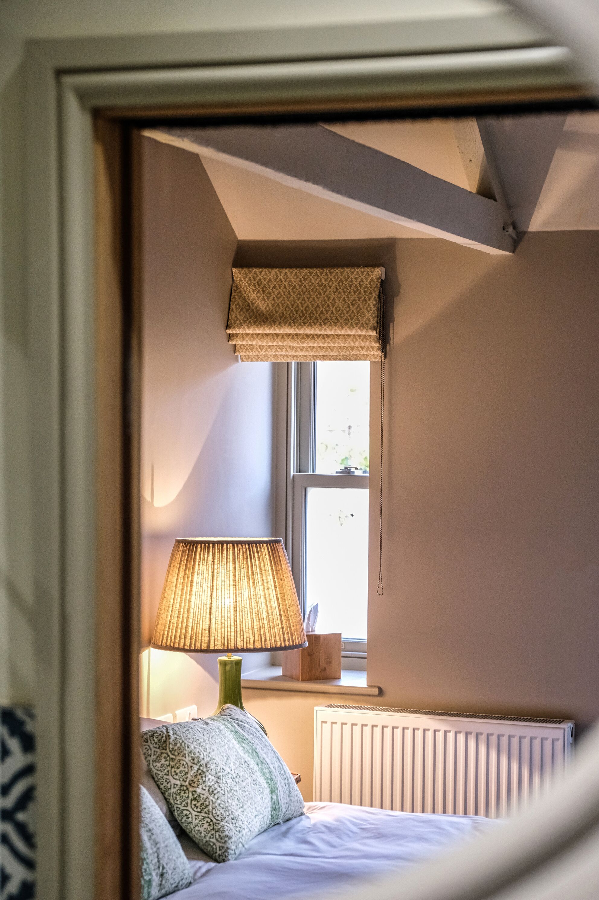 A bedroom with a bed, a bedside lamp, a window with a blind, and a radiator.