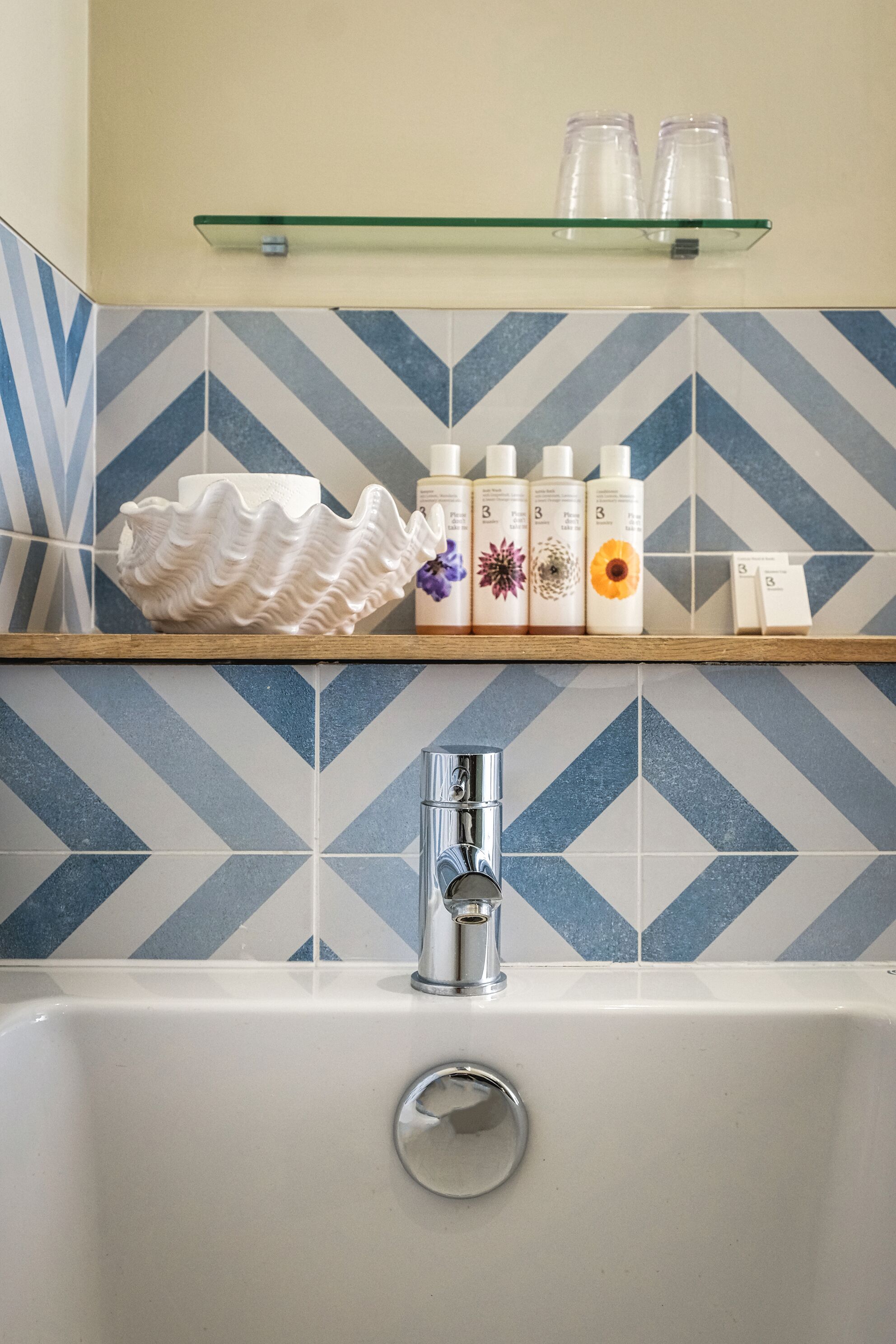 A bathroom with a white sink, a chrome faucet, and a shelf above holding toiletries and a decorative bowl.