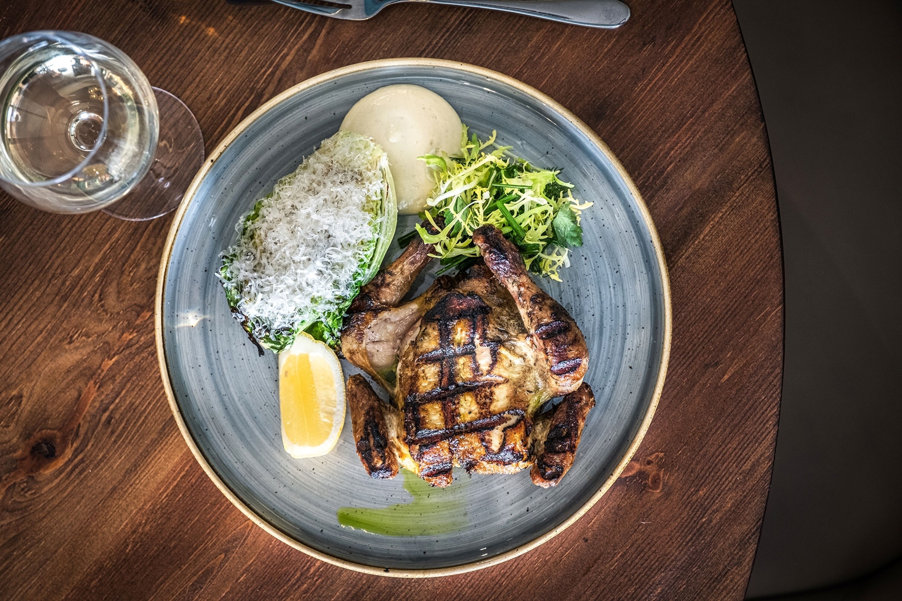 A plate with grilled chicken, mashed potatoes, and a side salad on a wooden table.